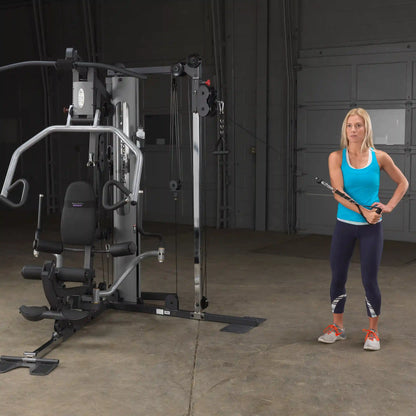 Woman using a Body-Solid home gym machine for cable exercises in a blue tank top.