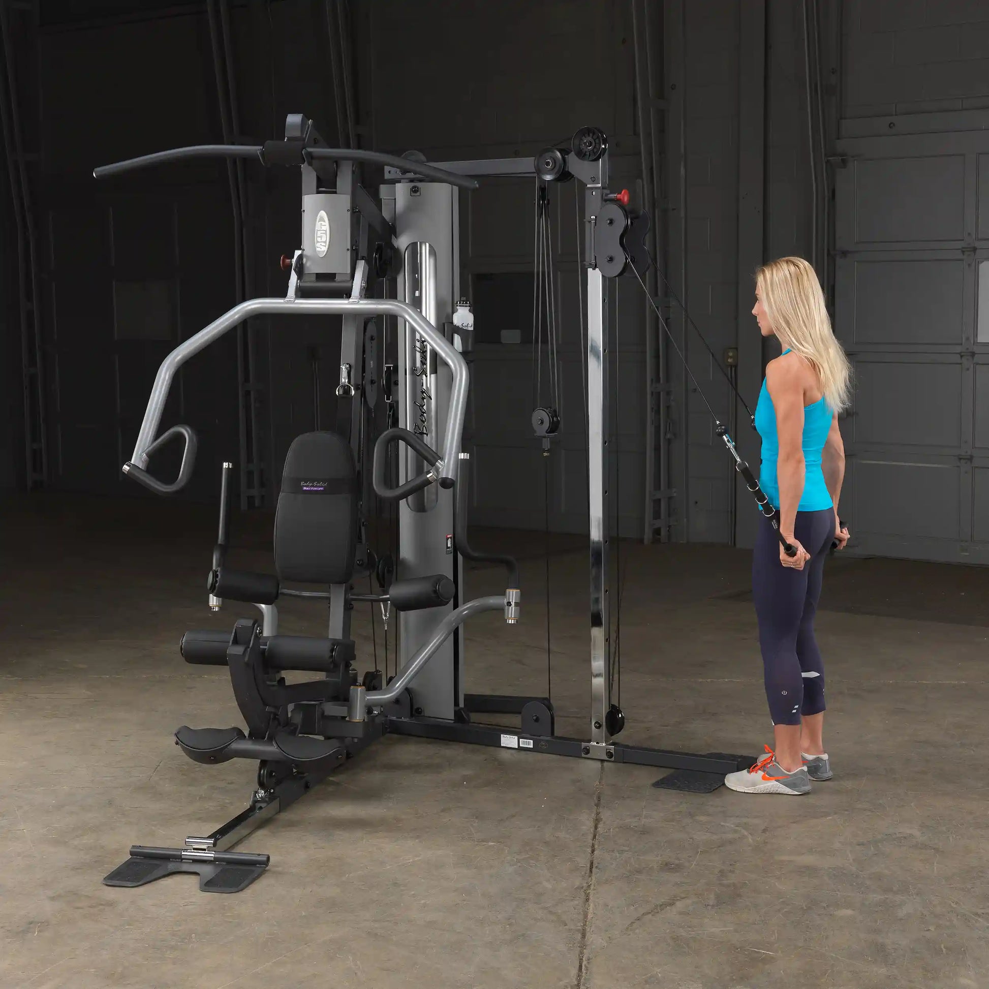 Woman using Body-Solid home gym machine with cable attachments in a workout session.