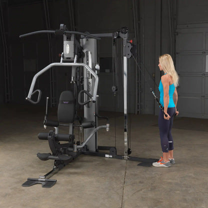 Woman using Body-Solid home gym machine with cable attachments in a workout session.