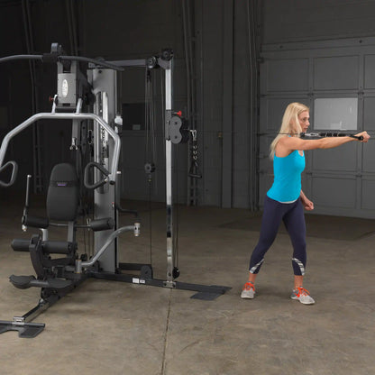 Woman using a Body-Solid home gym in a blue tank top, performing a cable exercise.