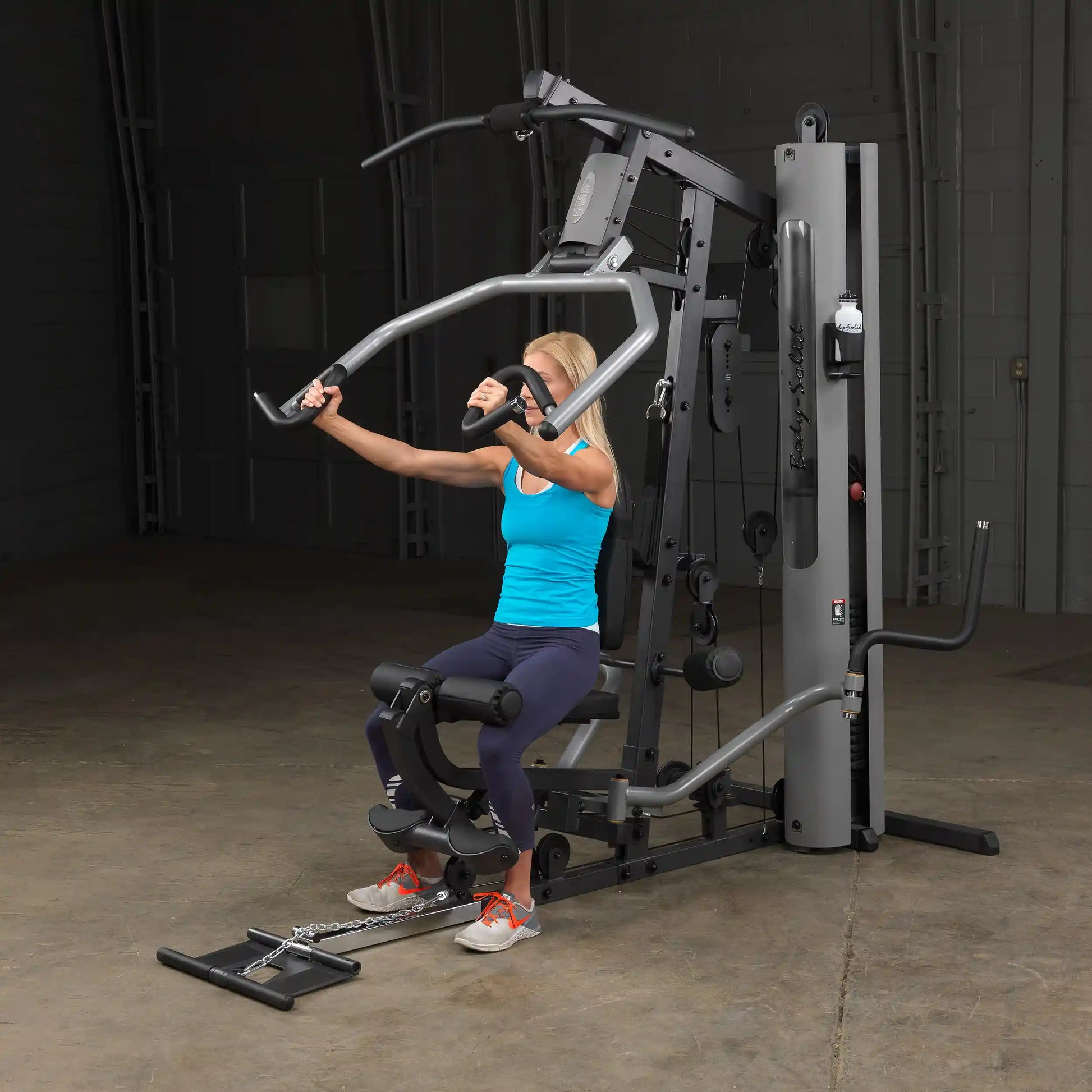 Woman using Body-Solid home gym in blue tank, performing chest press.