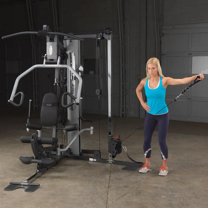 Woman using Body-Solid home gym in blue tank top, demonstrating cable exercise.