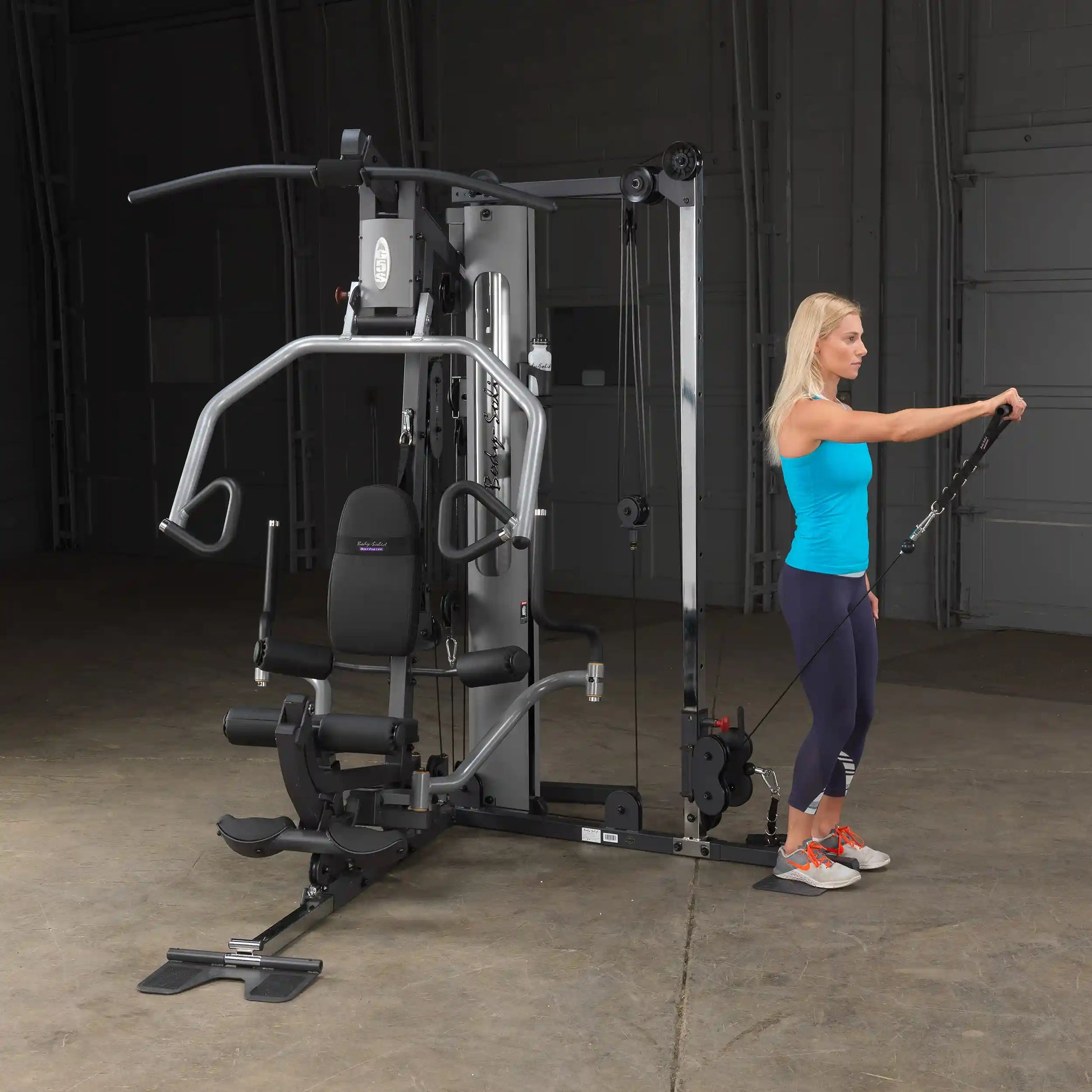 Woman using a Total Gym home workout machine with cable pulleys in a fitness studio.