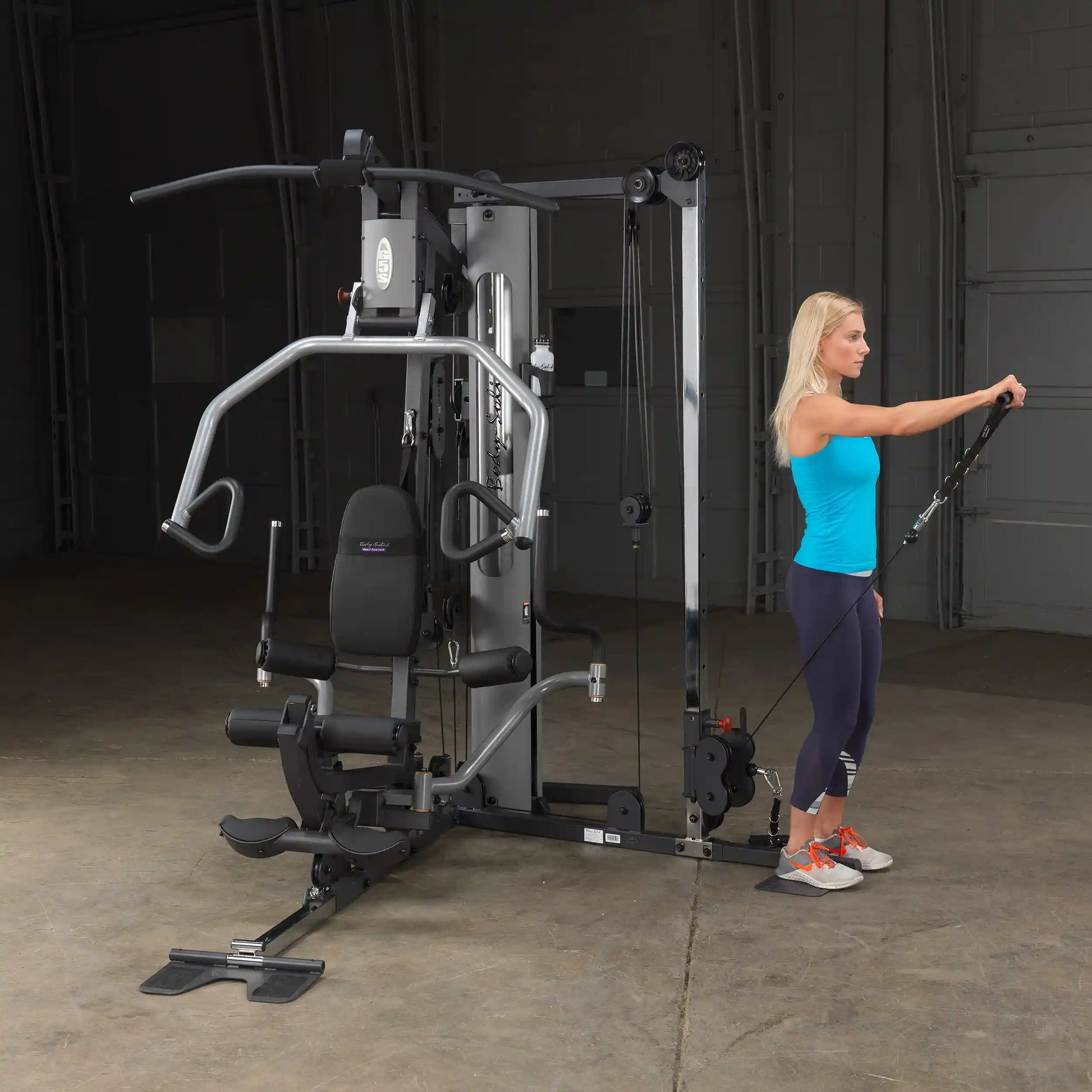 Woman using Body-Solid home gym machine with cable for strength training in a spacious room.
