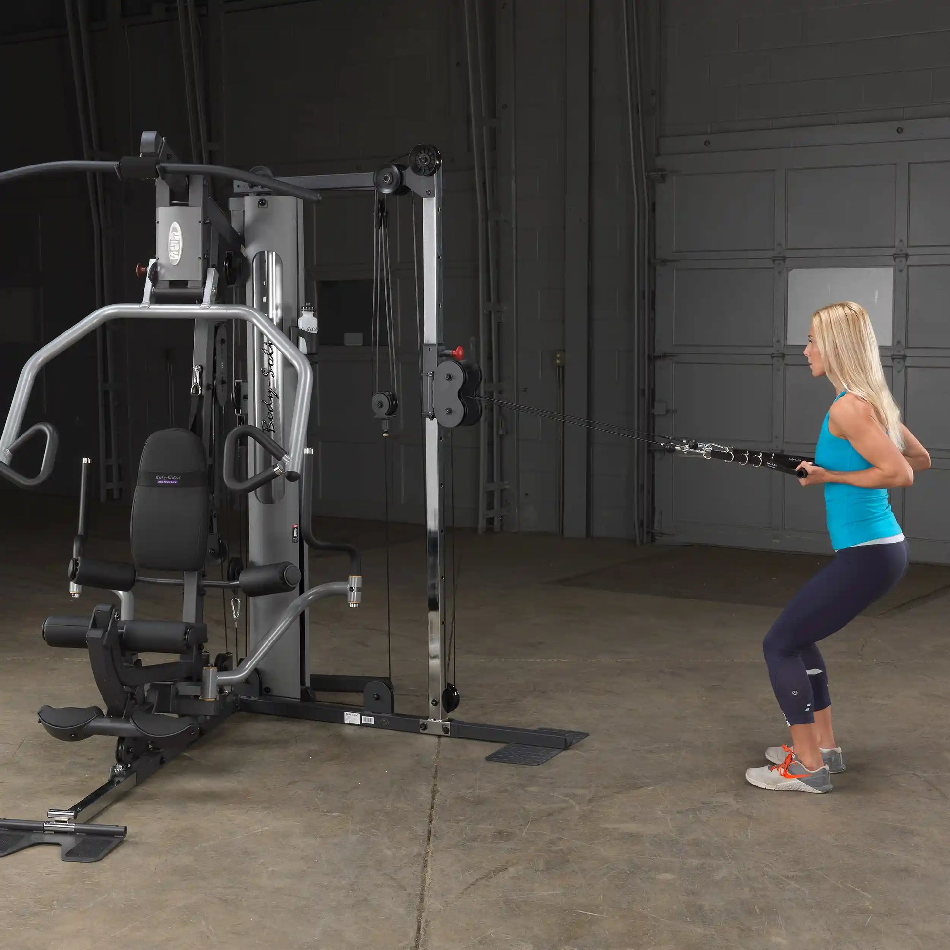 Woman using Body-Solid home gym for cable exercises in a garage.