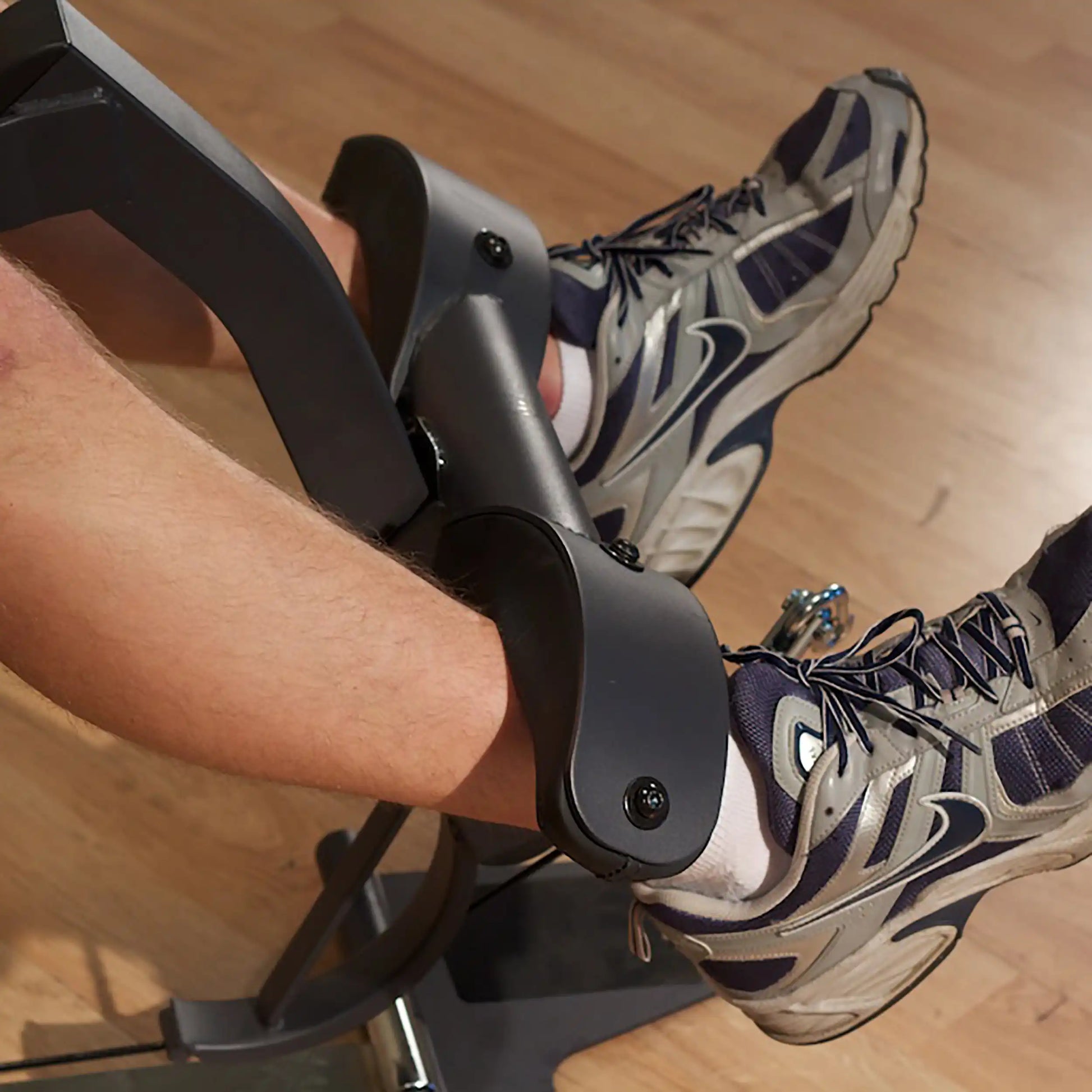 Legs in inversion table boots with gray sneakers on wooden floor.