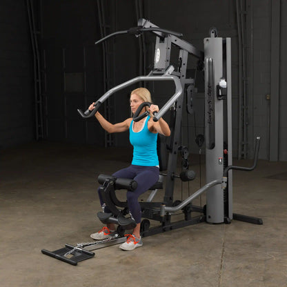 Woman using Body-Solid home gym in blue top for strength training.
