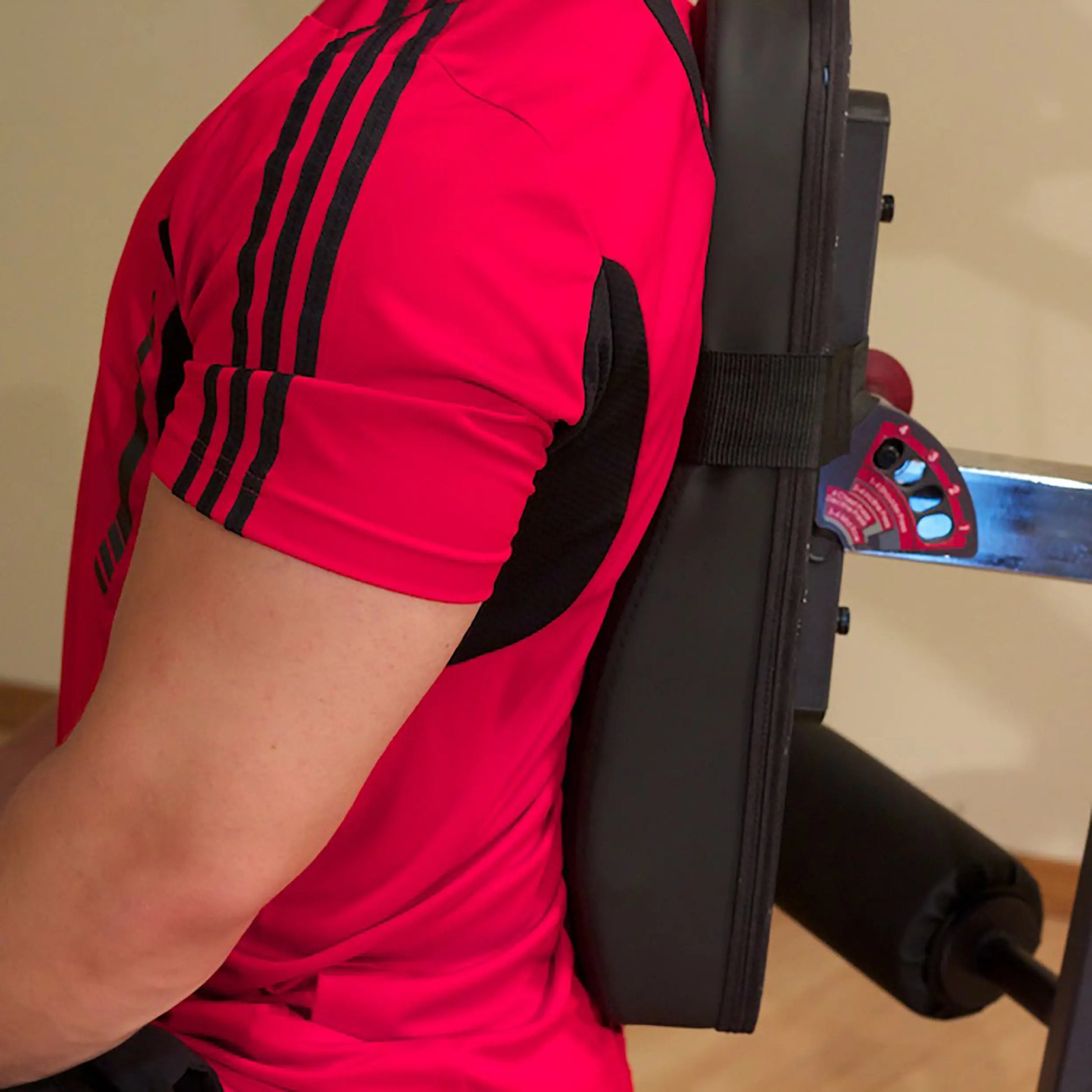 Man in red sports shirt using black padded gym equipment.
