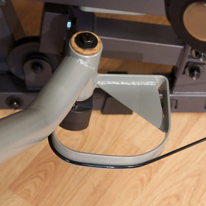 Gray metal hinge mechanism on wooden floor, featuring a bolt and bracket design.