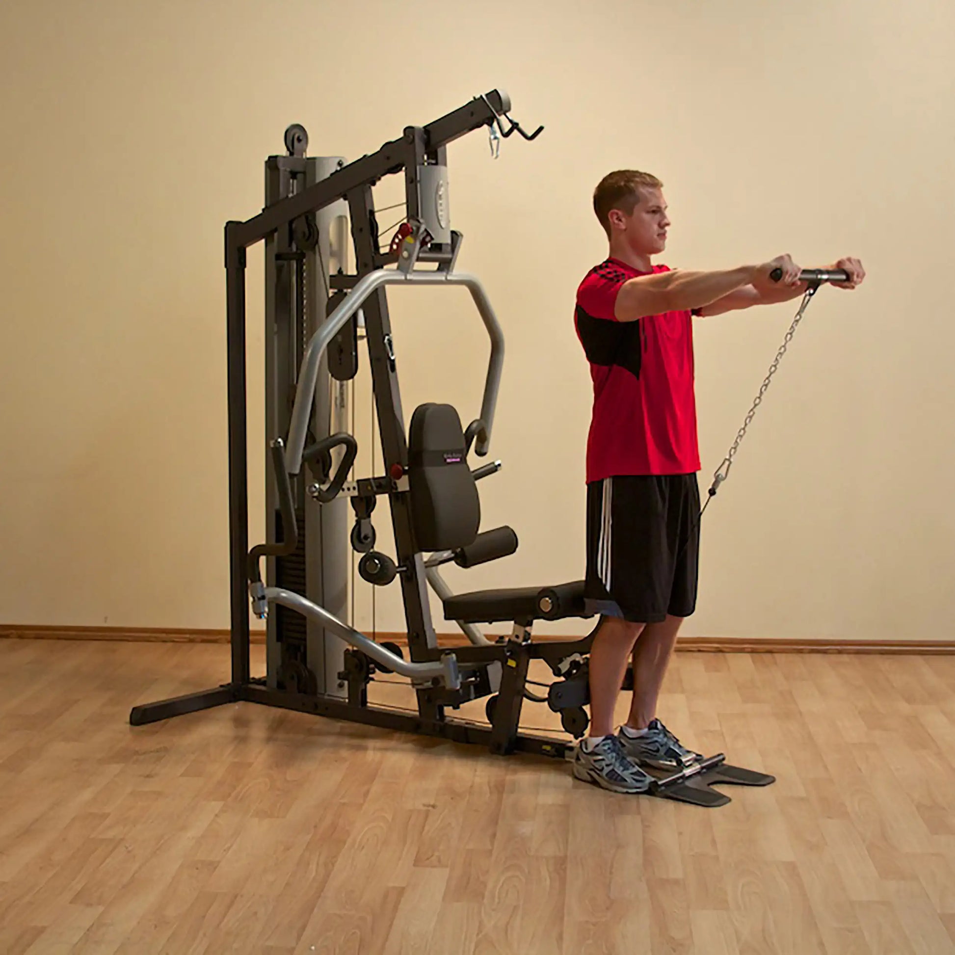 Man using a multi-gym machine in a red shirt, demonstrating strength training exercises.
