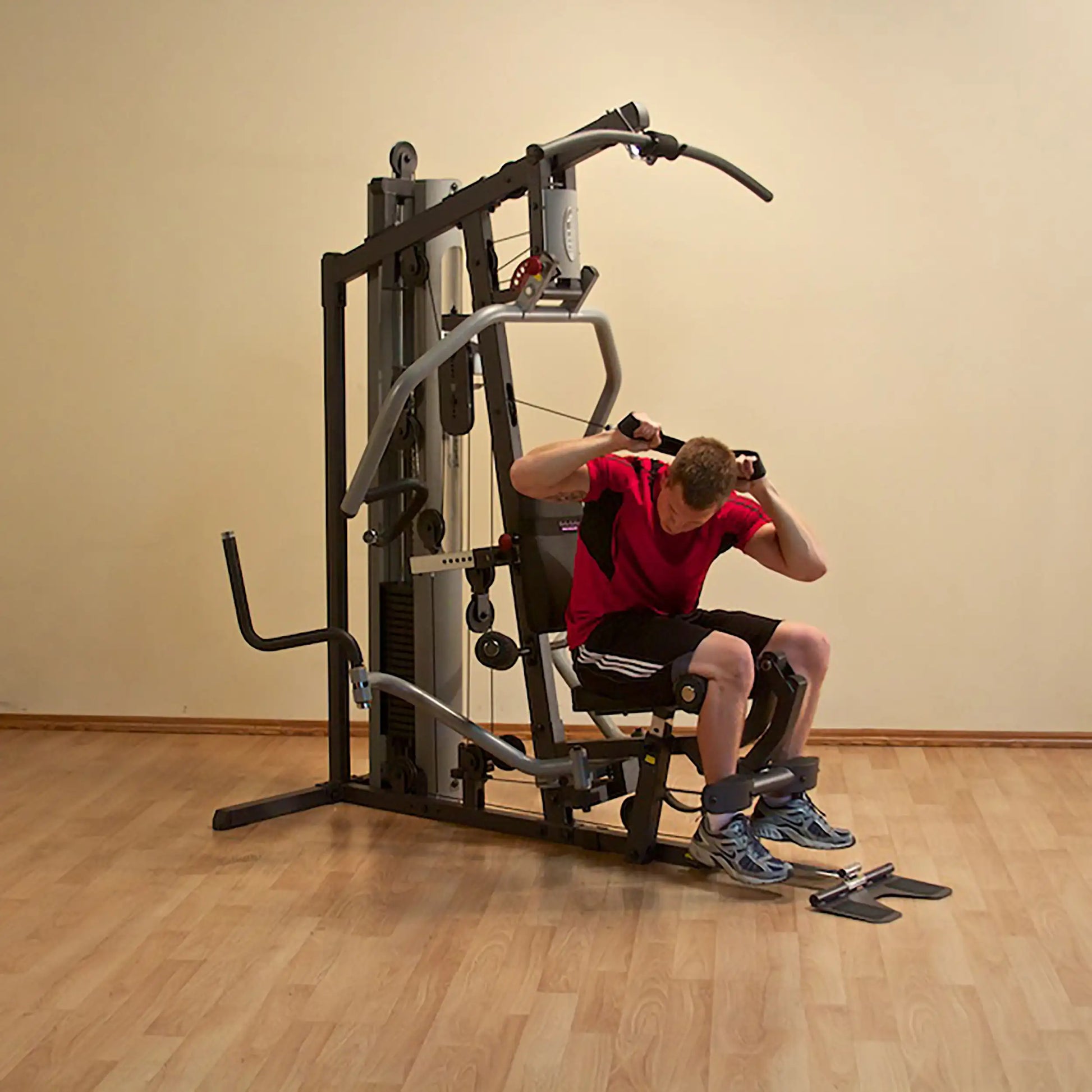 Man using a multi-station home gym in a red shirt, performing a strength workout.