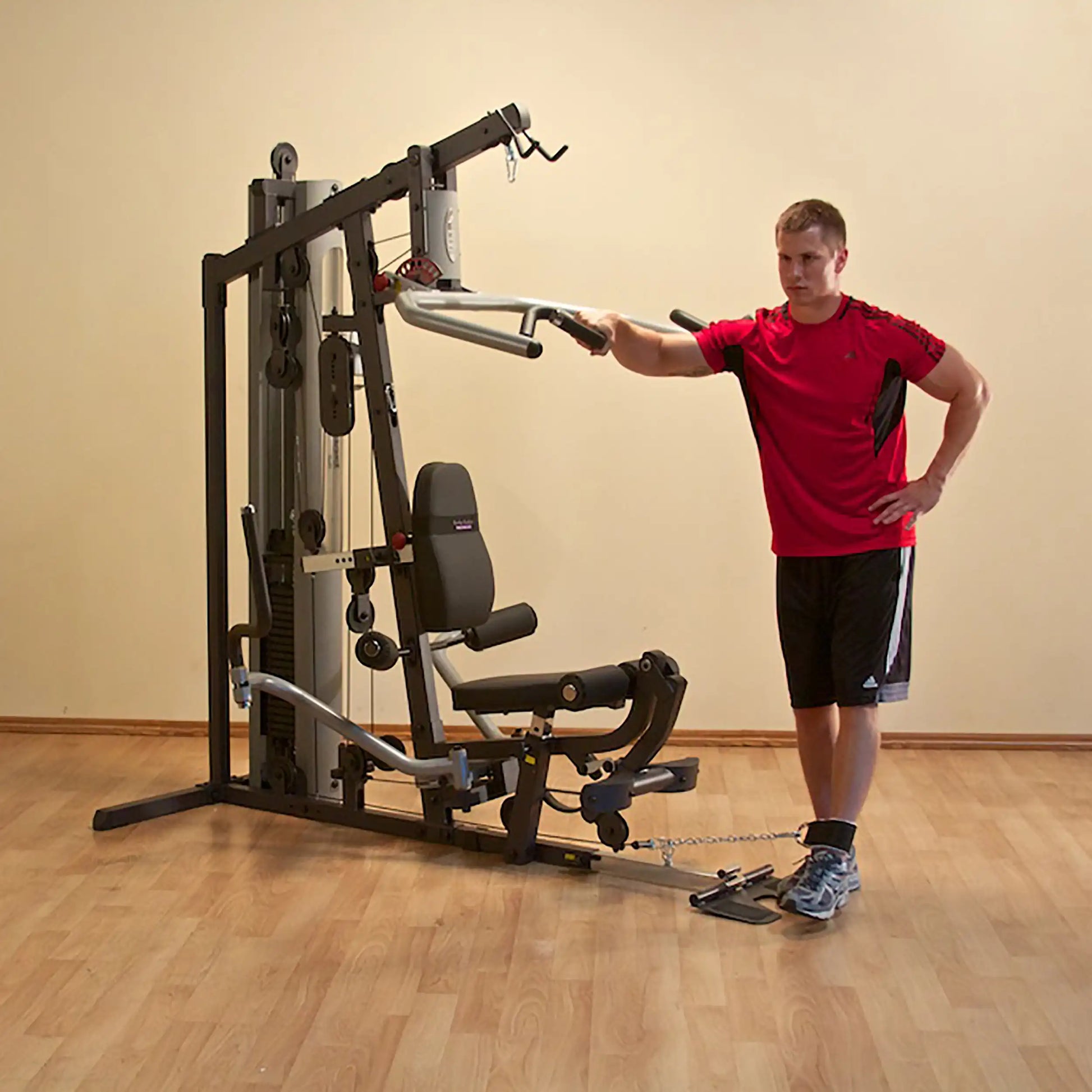 Man using multi-gym machine in red shirt and black shorts for workout in home setting.