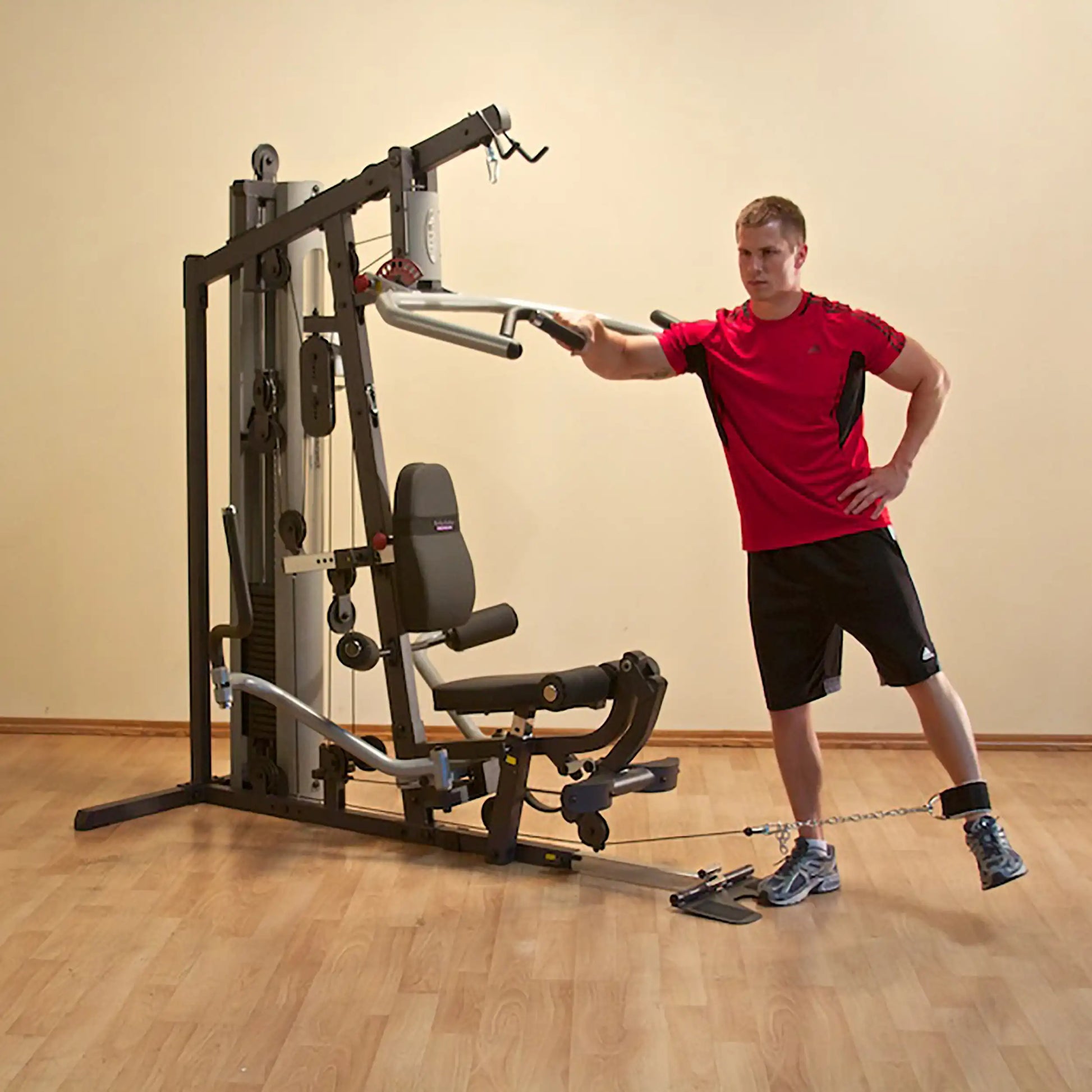 Man exercising on a multi-station home gym in a red shirt and black shorts.