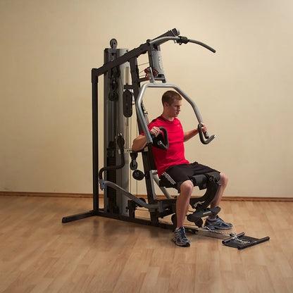Man using a multi-station home gym in red shirt and black shorts.