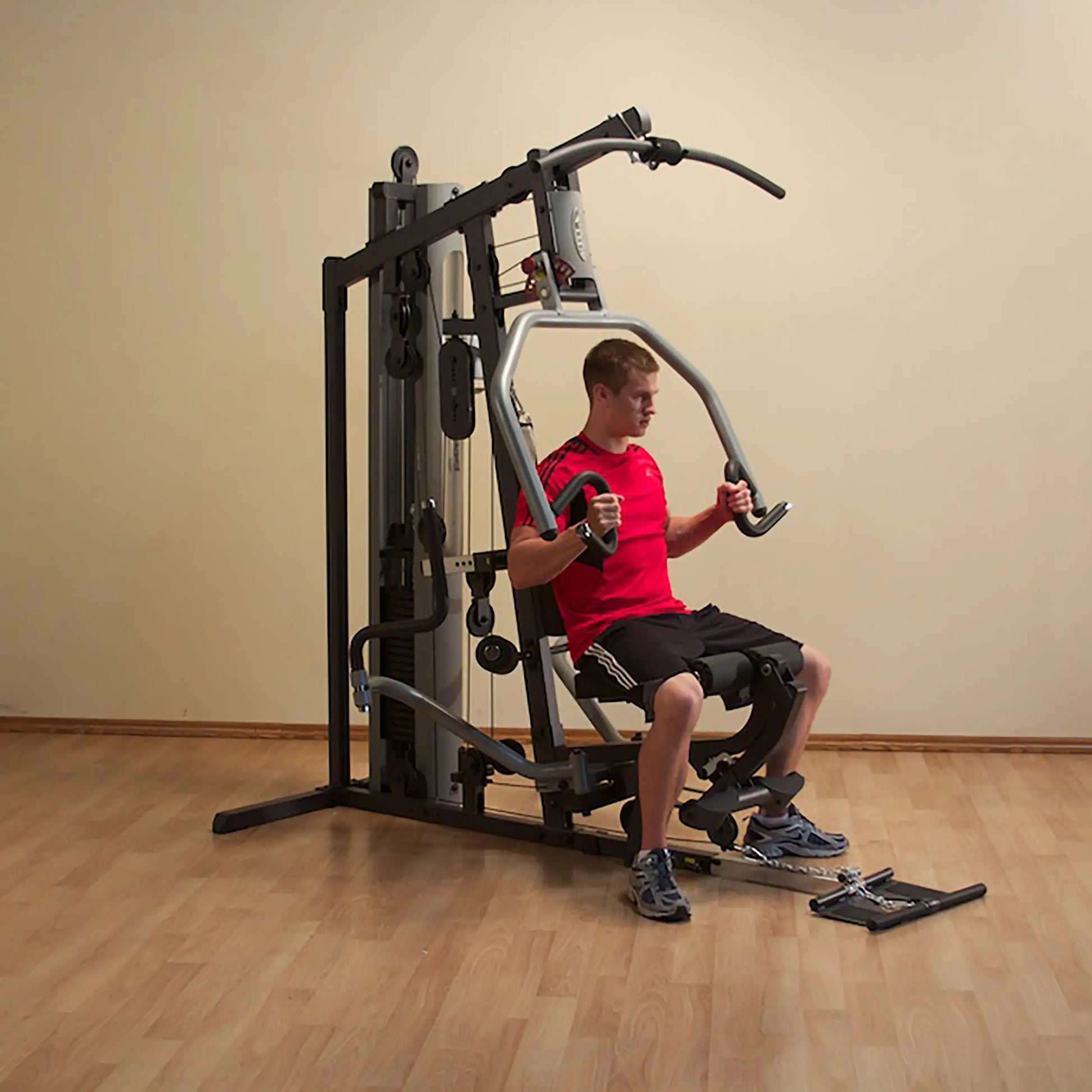 Man using a multi-station home gym in a red shirt for strength training.