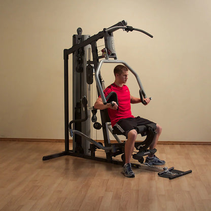 Man using home gym machine in red shirt, performing chest press on wooden floor.