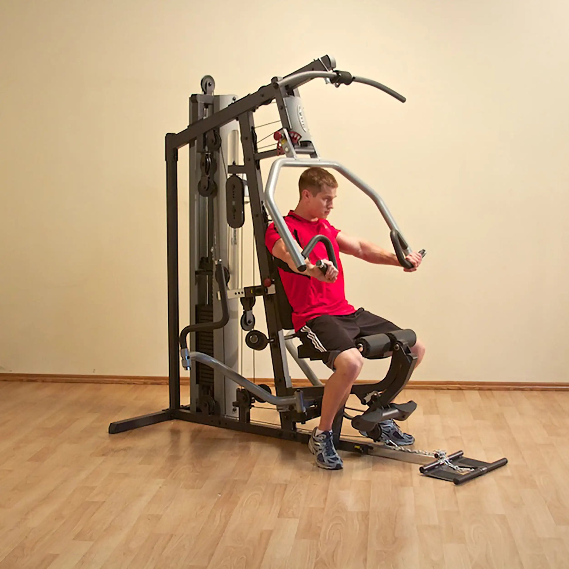 Man using a home gym machine in a red shirt, exercising on wooden flooring.