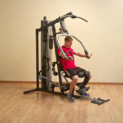 Man using a home gym machine in a red shirt, exercising on wooden flooring.