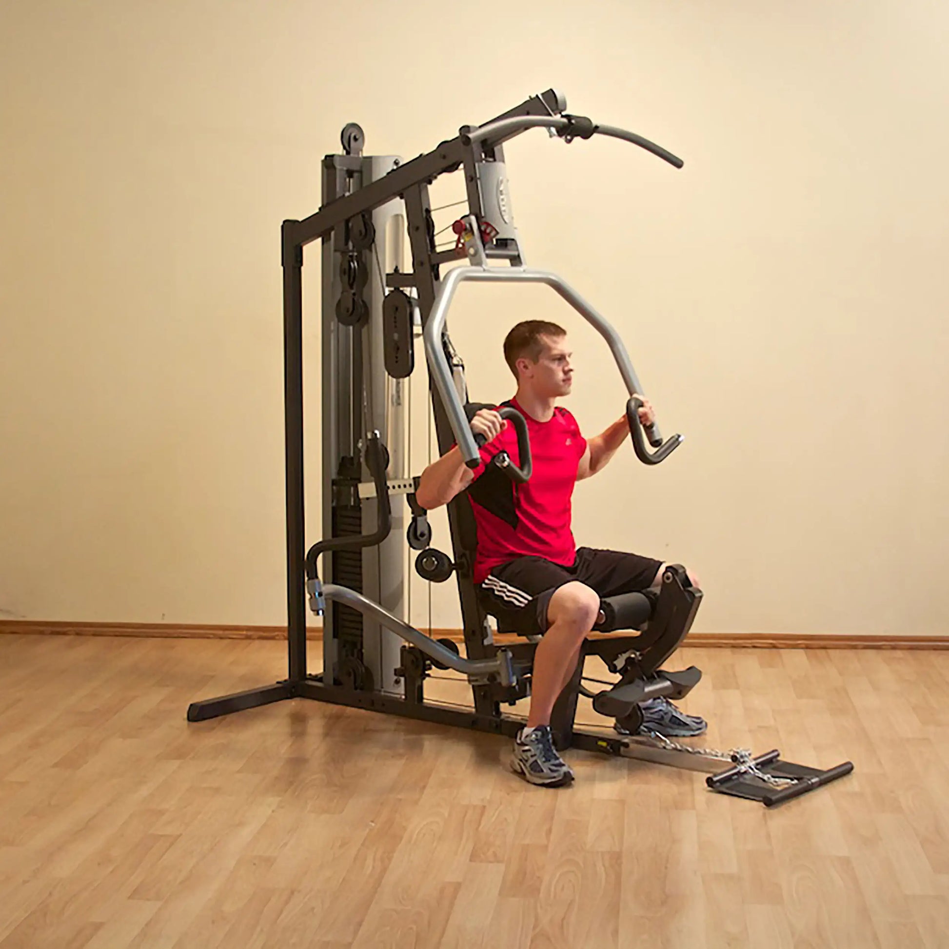 Man using a home gym machine in a red shirt on wood flooring.