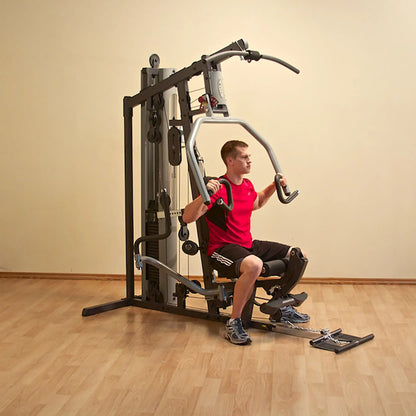 Man using a home gym machine in a red shirt on wood flooring.
