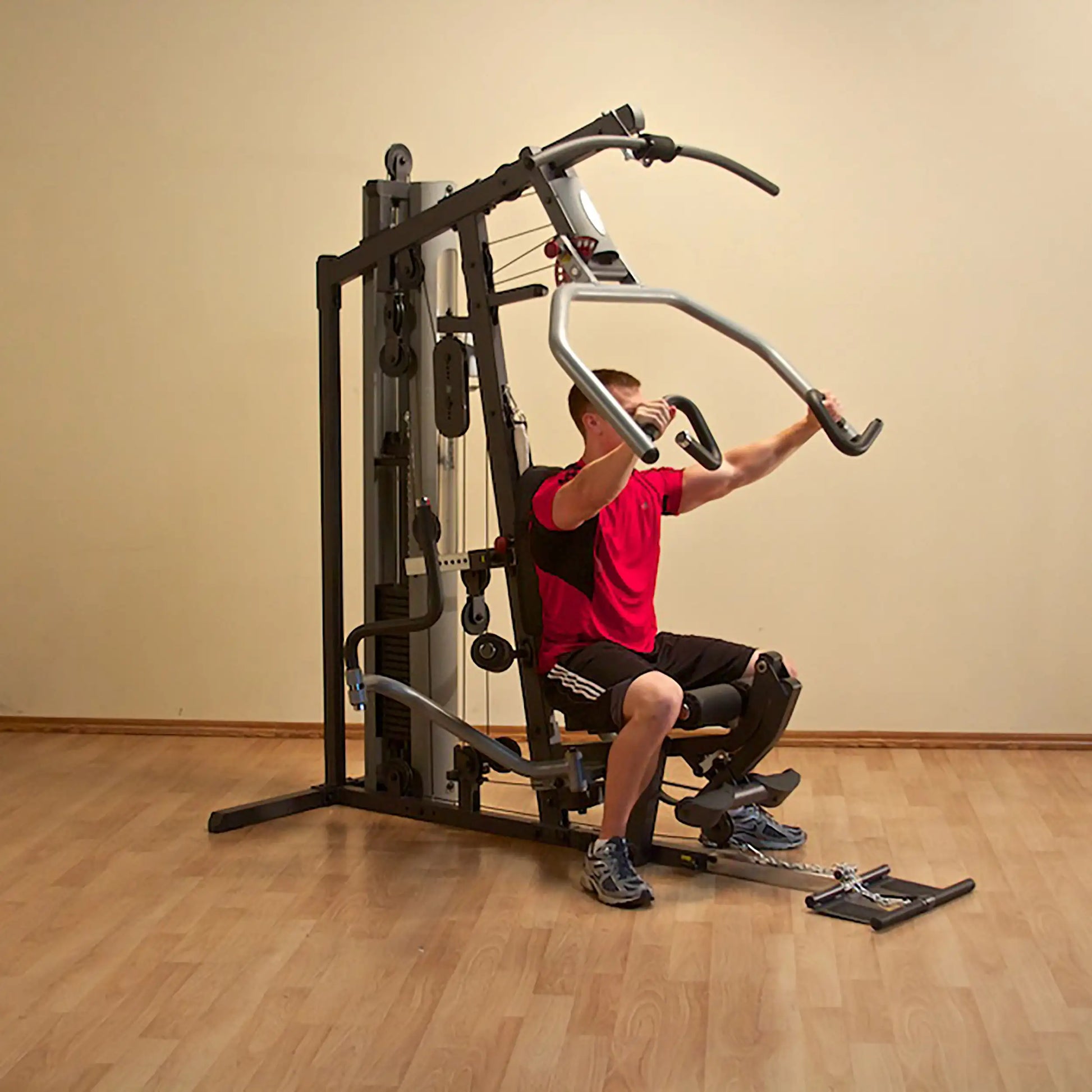 Man using multi-exercise gym machine in red shirt on wooden floor.