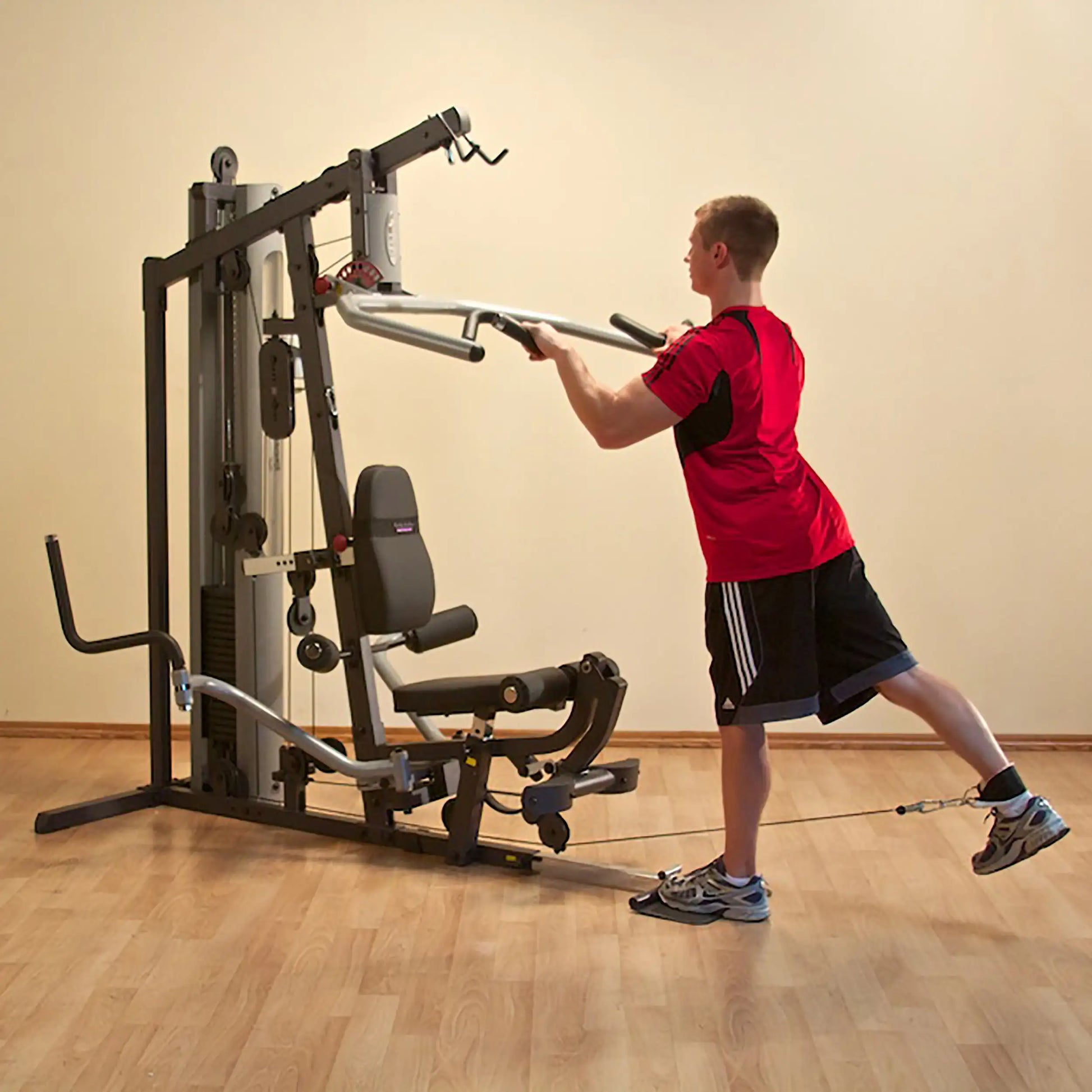 Man using a Bowflex home gym for leg exercise in a red shirt.