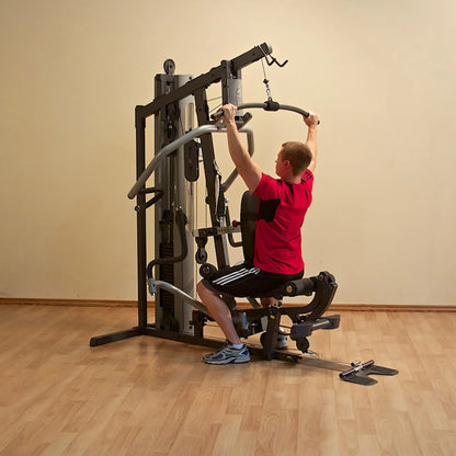 Man using a home gym machine in a red shirt on wooden floor.
