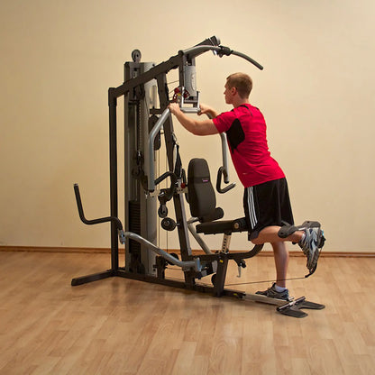 Man using a multi-function home gym machine in a red shirt, performing leg exercises on hardwood floor.