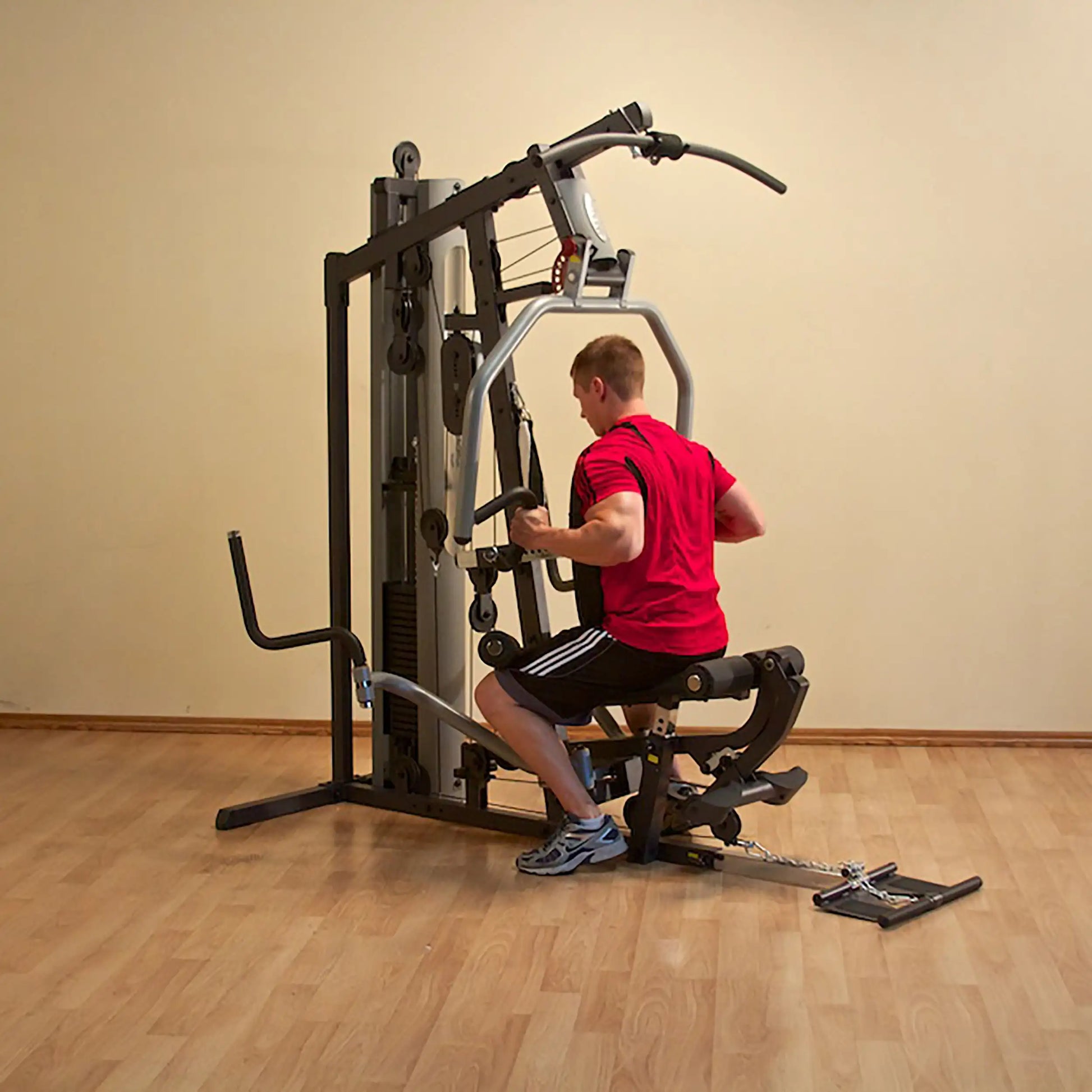 Man using a home gym machine in a red shirt on wooden flooring.