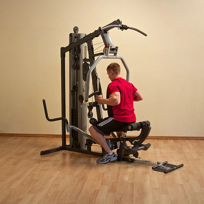 Man using a home gym machine in a red shirt on wooden flooring.