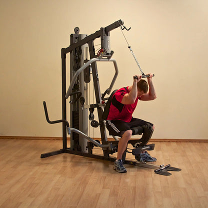 Man using a multi-function weight machine in a gym, performing seated exercises in a red shirt.