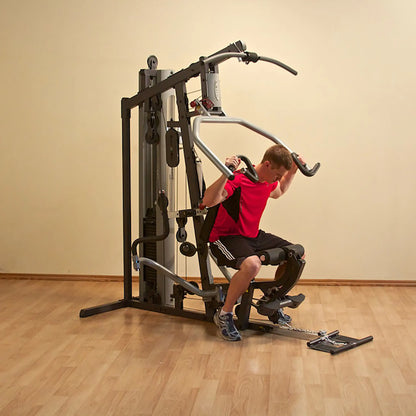 Man exercising on a home gym machine with a red shirt, using the lat pulldown feature for strength training.