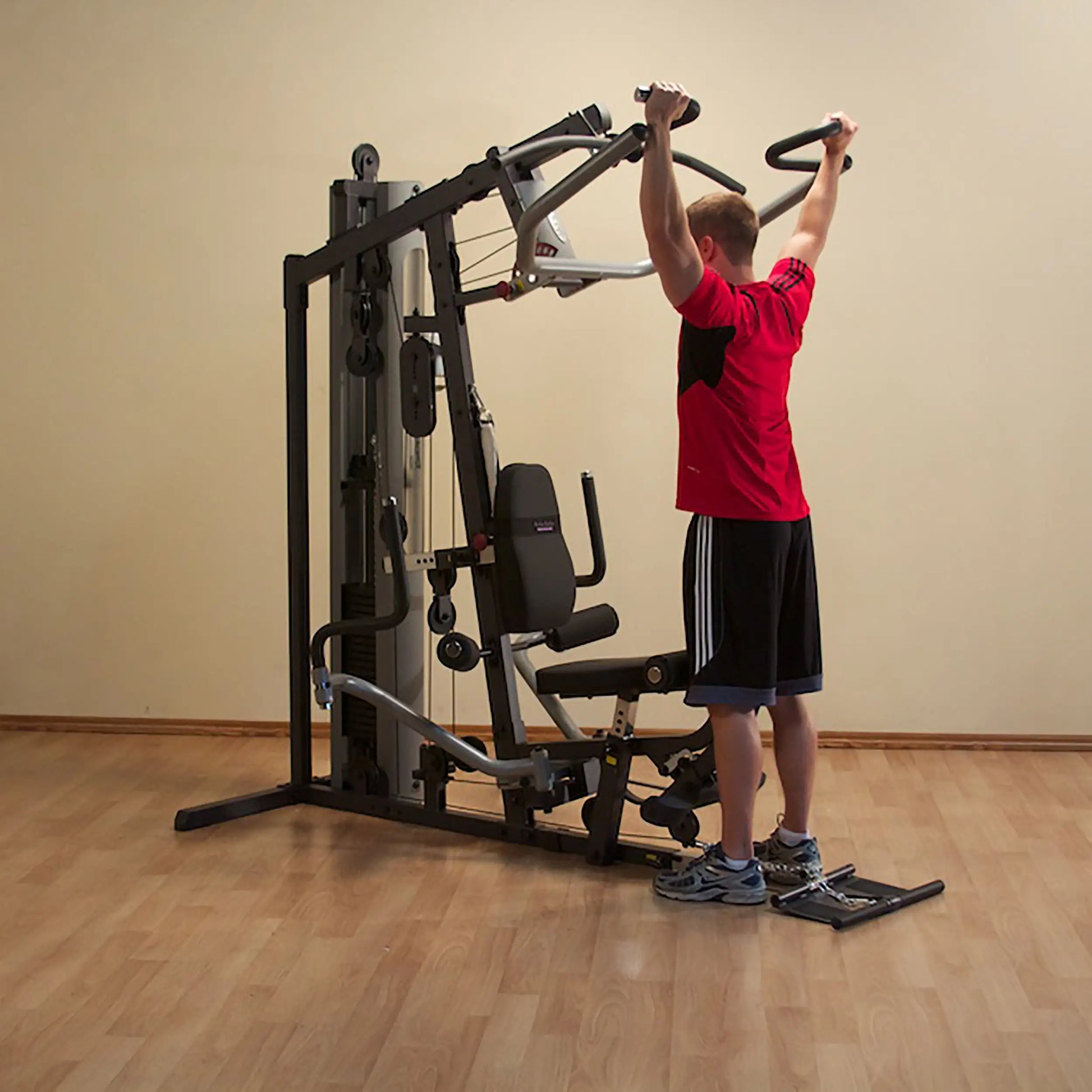 Man using a home gym machine in a red shirt, performing an overhead press.