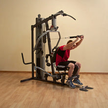 Man using multi-gym machine in red shirt for strength training on wooden floor.