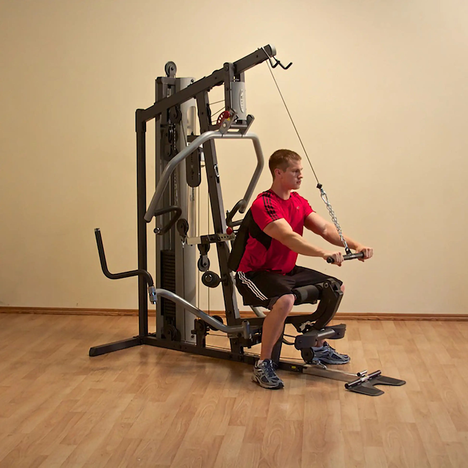 Man using a home gym machine with cable row in red shirt and black shorts.