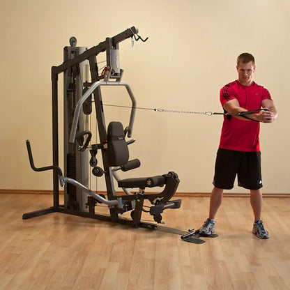 Man using multi-gym machine in red shirt for strength training on wooden floor.