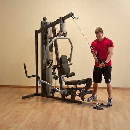 Man using a home gym machine for cable exercises, wearing a red shirt in a wooden floored room.