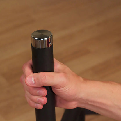 Hand gripping a black metal walking cane with a chrome handle on a wooden floor.
