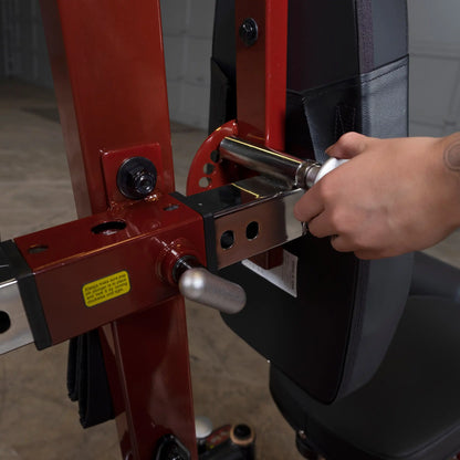 Adjusting red power rack safety bar with secure locking pin for gym equipment setup.