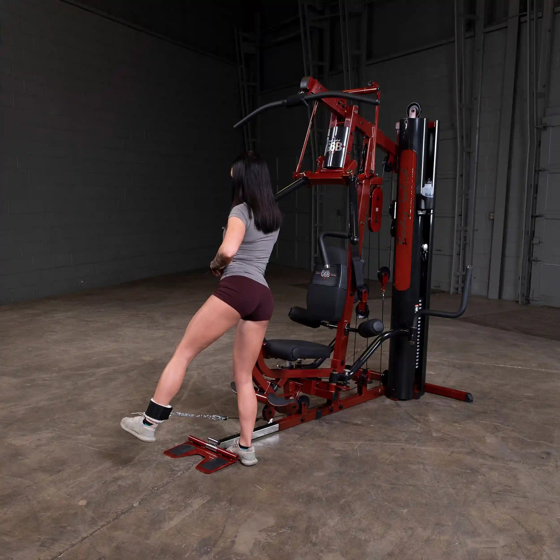 Woman using a red home gym machine for leg exercise.