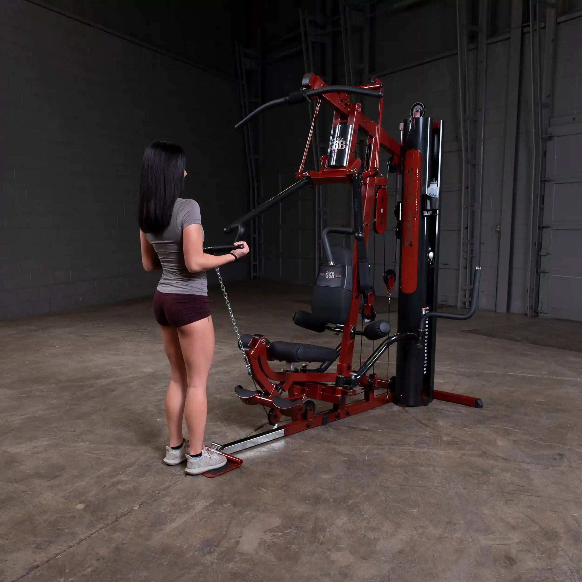 Woman using Body-Solid home gym with red frame in a spacious room.