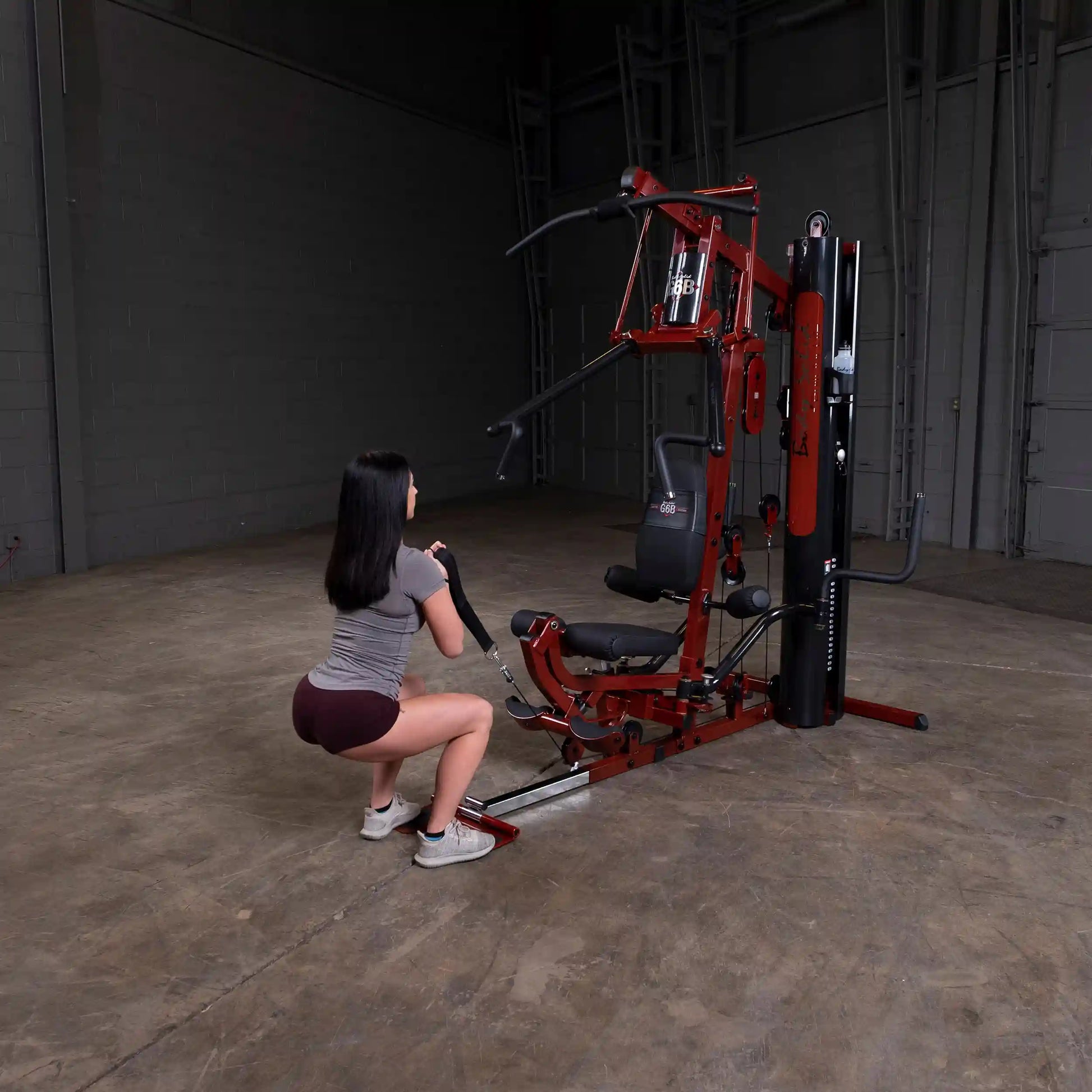 Woman using maroon Bowflex home gym for squats in a spacious room.