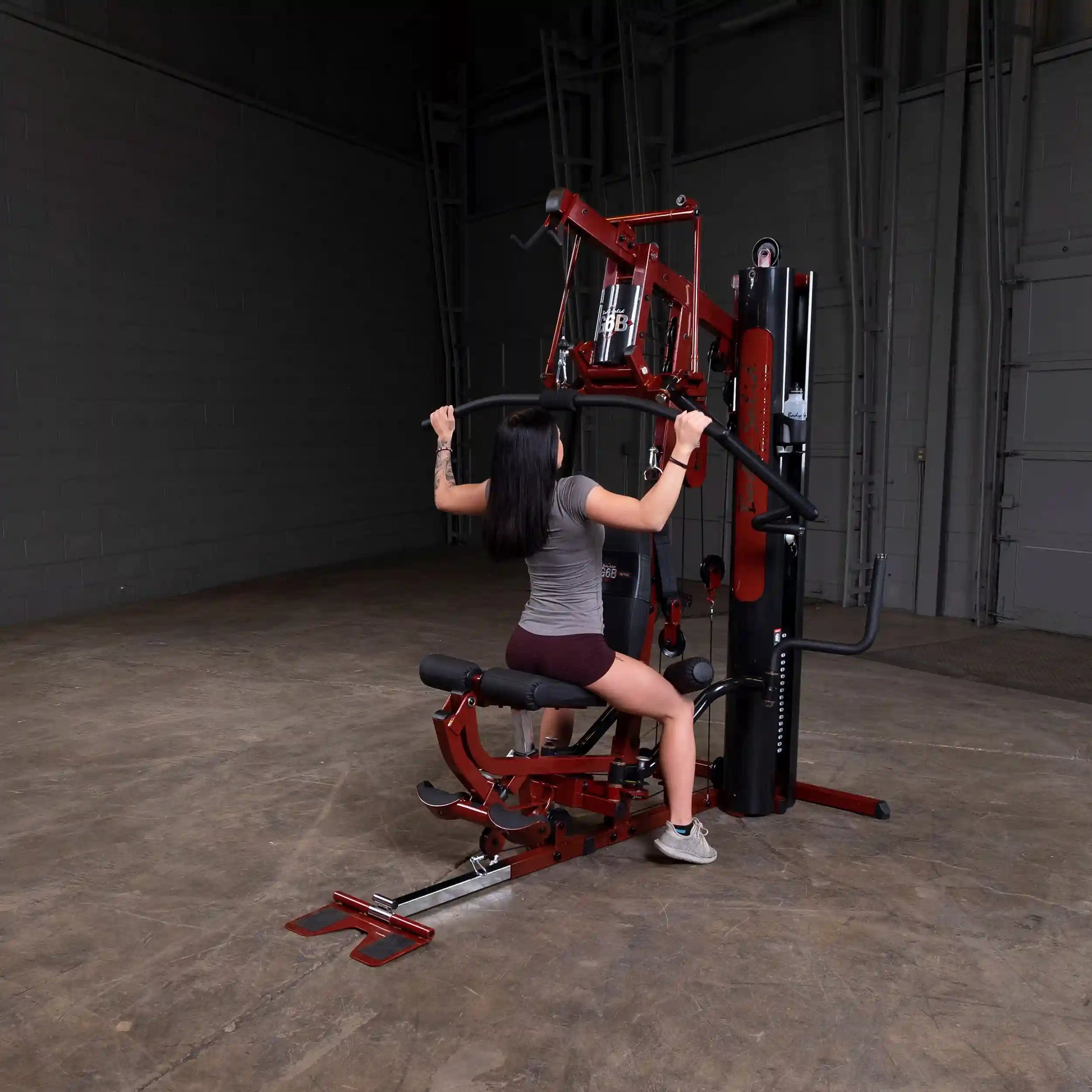 Woman using a red Body-Solid home gym machine for strength training.