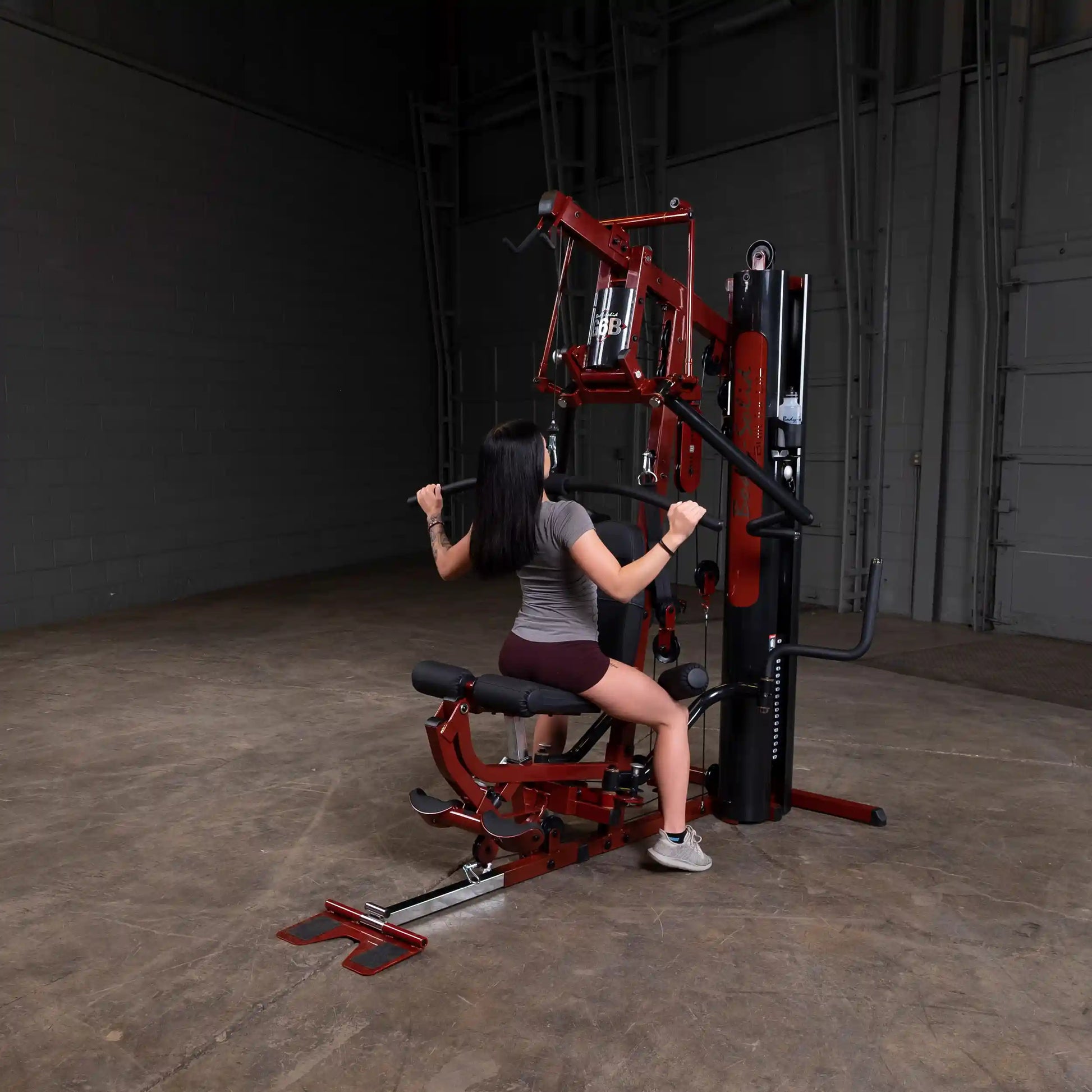 Woman using red Body-Solid home gym machine for strength training.