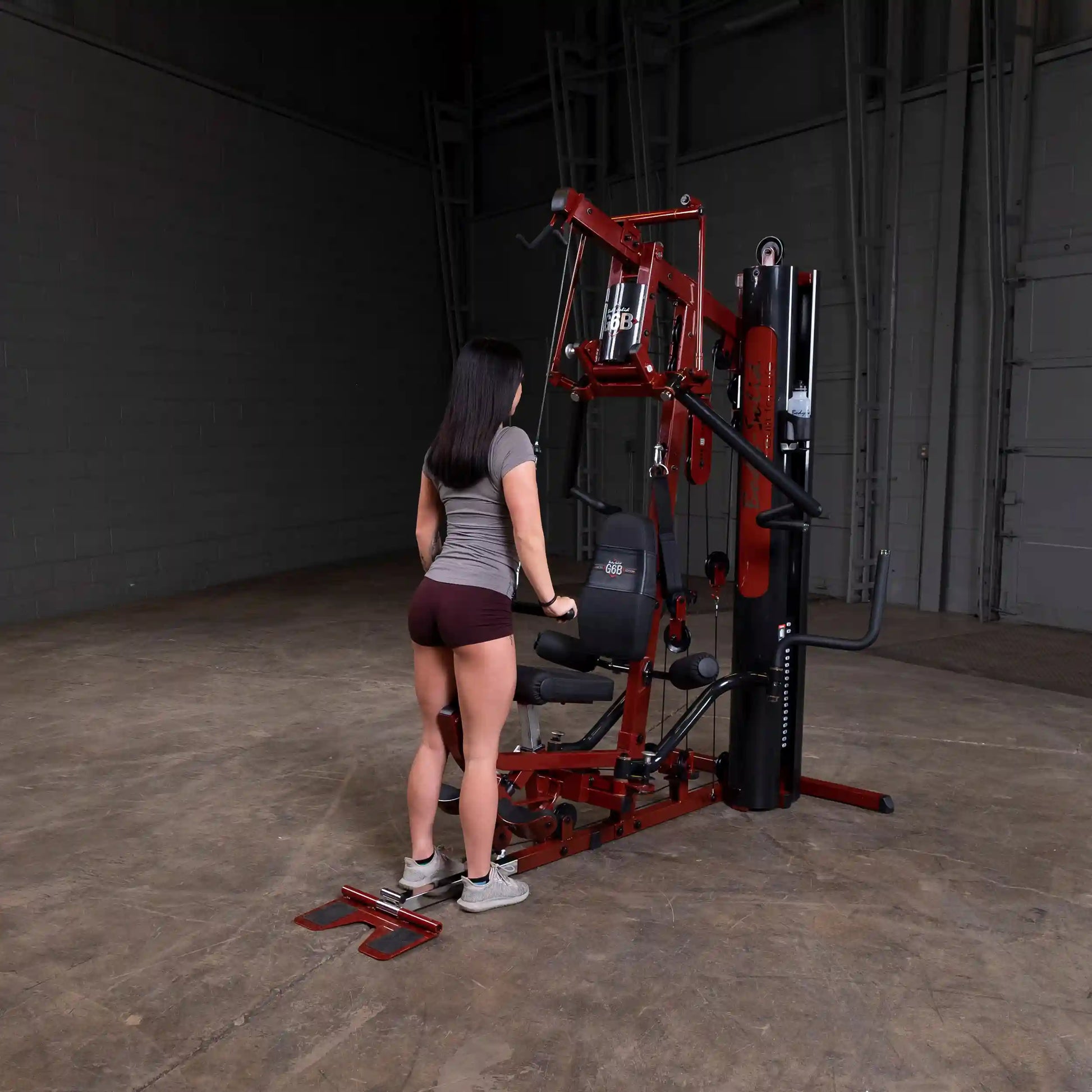 Woman using red Body-Solid home gym machine in a dimly lit room.