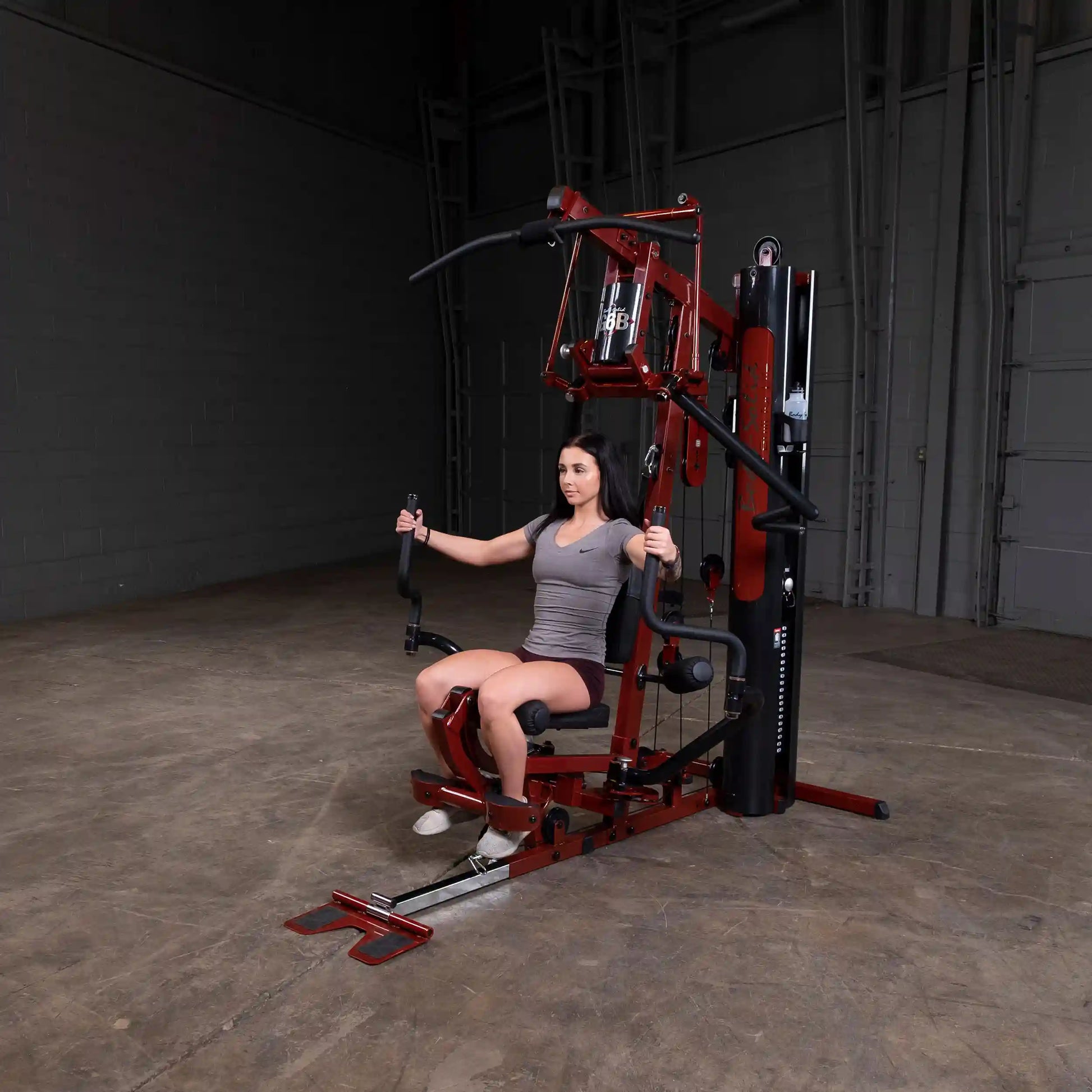 Woman using Body-Solid home gym in red for strength training.