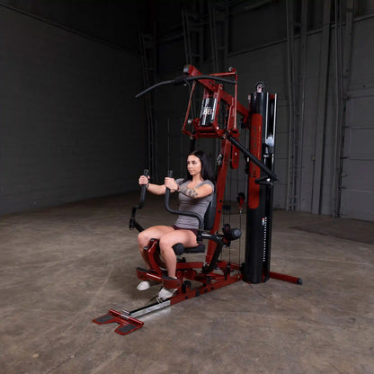 Woman using a red Body-Solid home gym machine with adjustable weights for strength training.