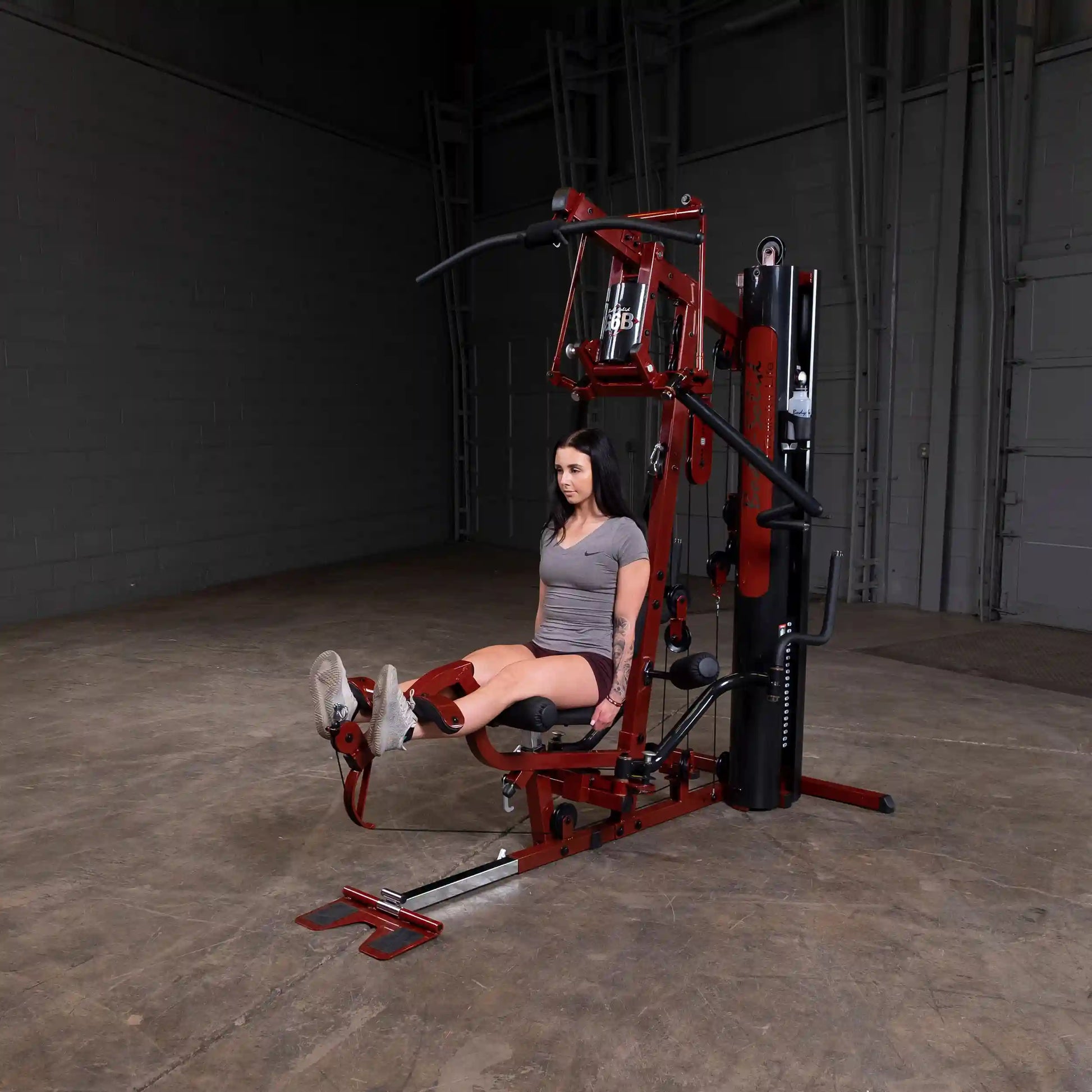 Woman using red home gym machine for leg exercises.