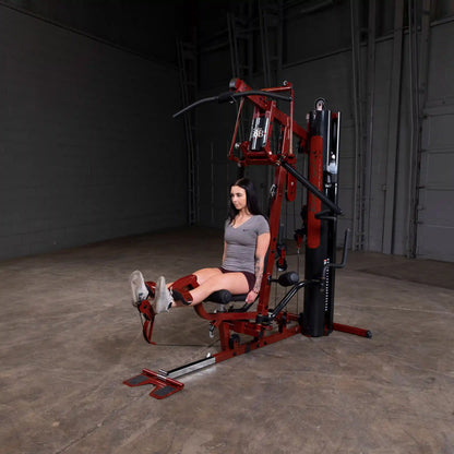 Woman using red home gym machine for leg exercises.