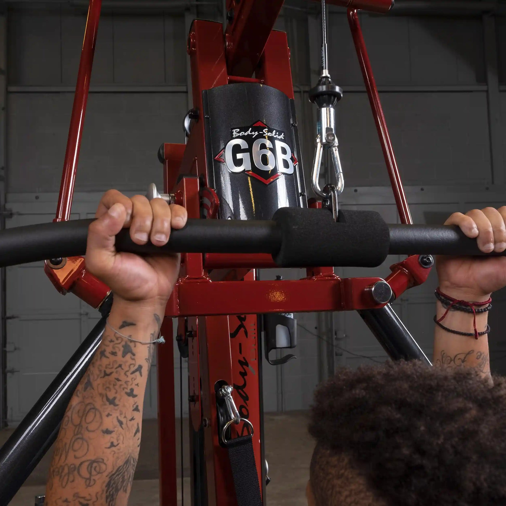 Body-Solid G6B gym machine with red frame and person gripping lat pulldown bar.